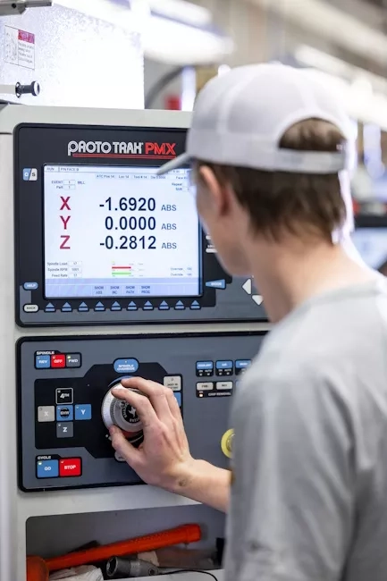 A student wearing a ballcap and operating a machine