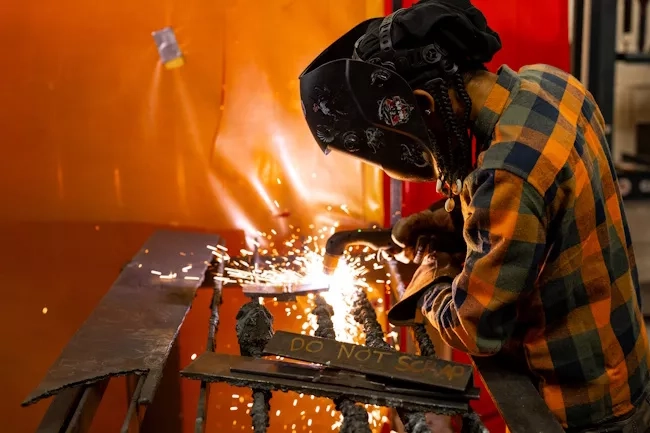 A person wearing welding protective gear and working on a piece of metal