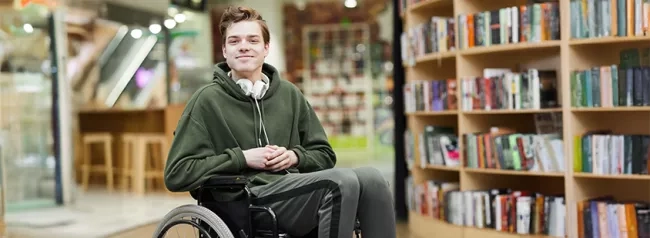 A man wearing a hoodie, seated in a wheelchair, and in a library