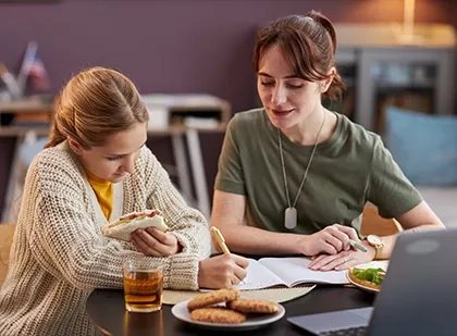 Two women seated at a table with a laptop in front of them, eating some snacks