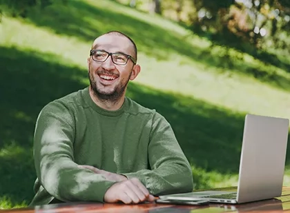 A man wearing a green shirt seated at a picnic table outside