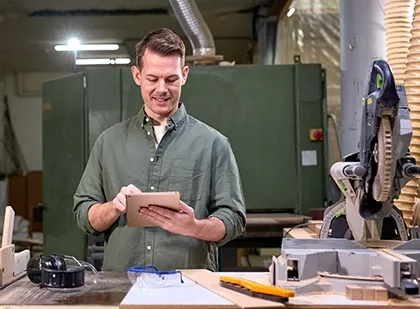 A man standing behind a desk in a work area holding a tablet
